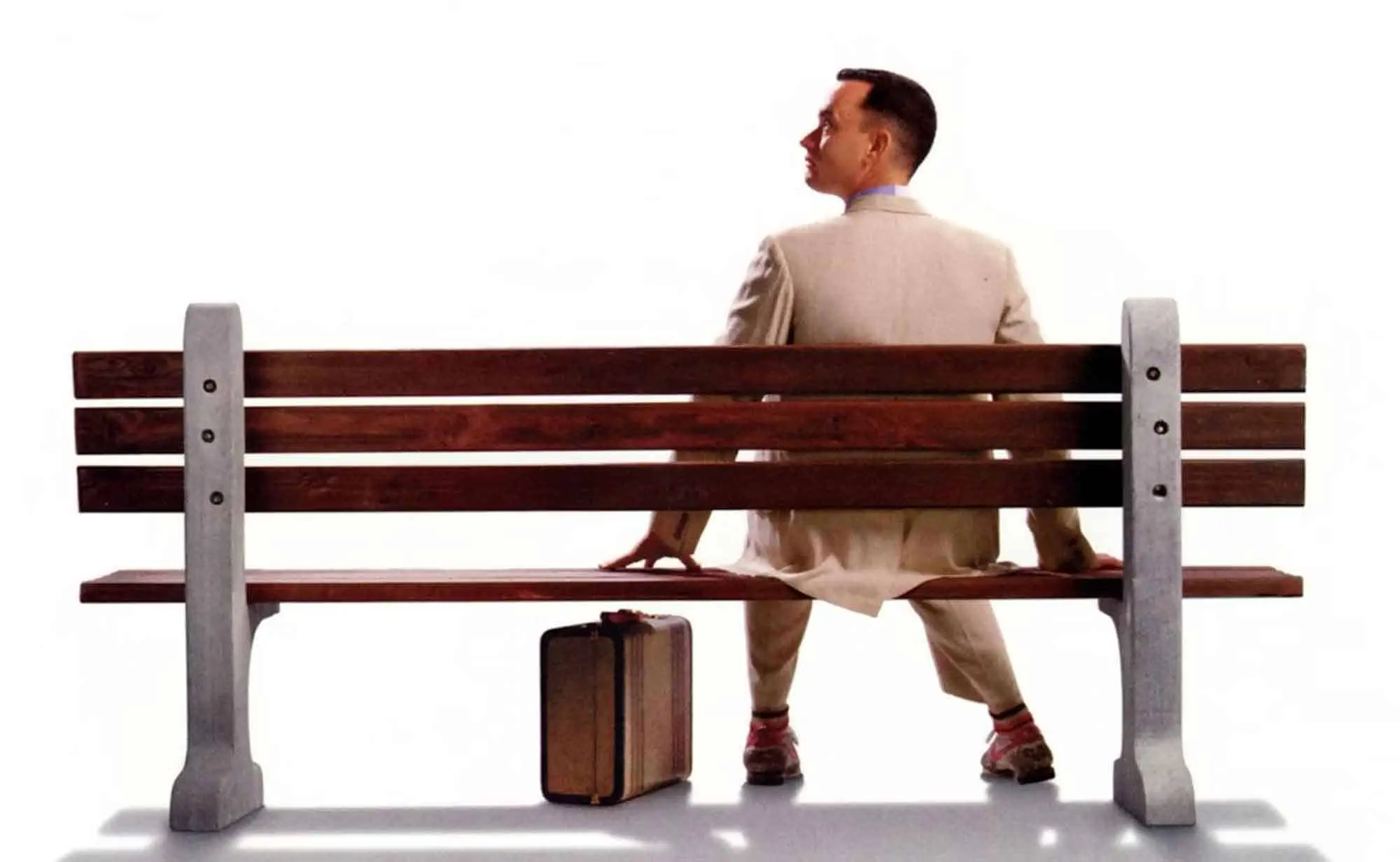 ALT: Man sitting on park bench with luggage, looking away, casual outfit, isolated background.