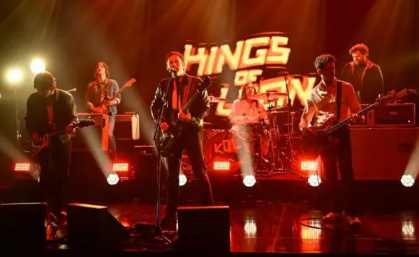 Energetic rock band on stage with colorful lights and "HINGS of THE" backdrop.