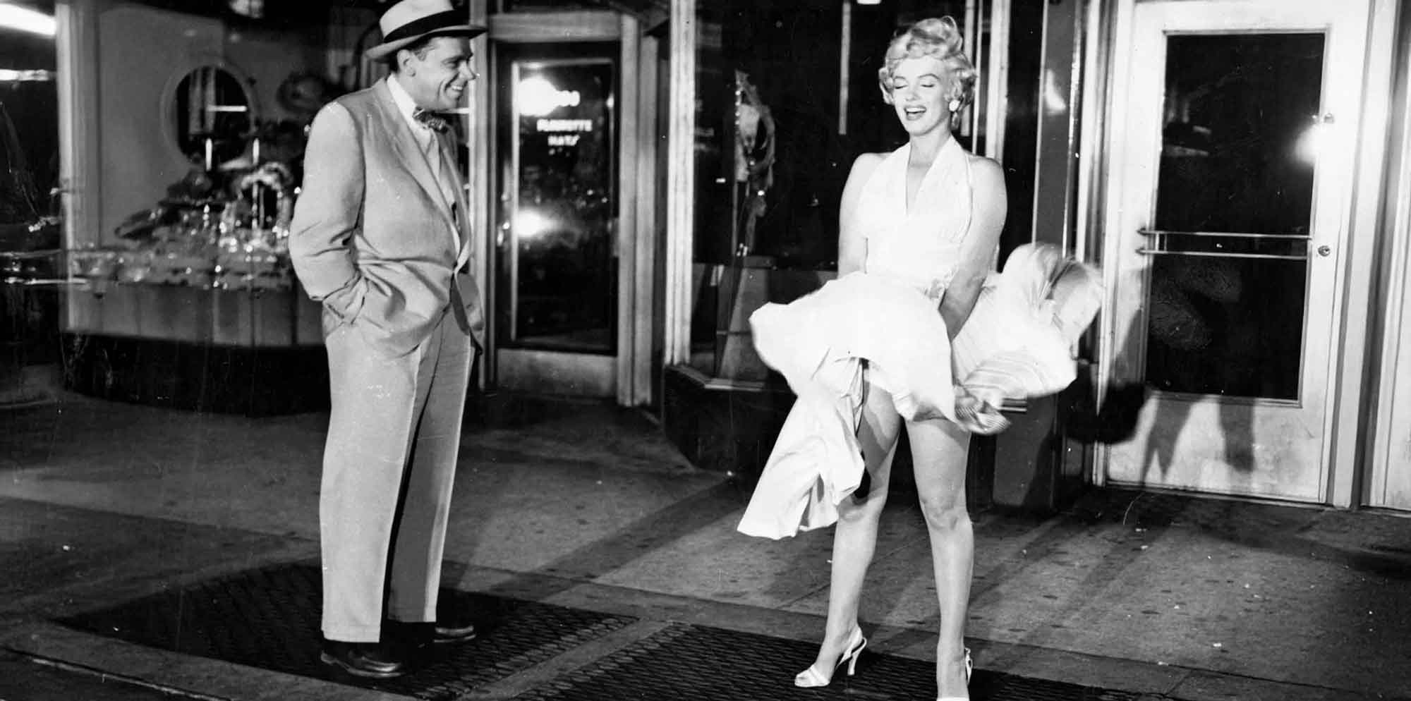 Vintage black and white photo of a woman in glamorous dress and high heels talking to a man in a suit.