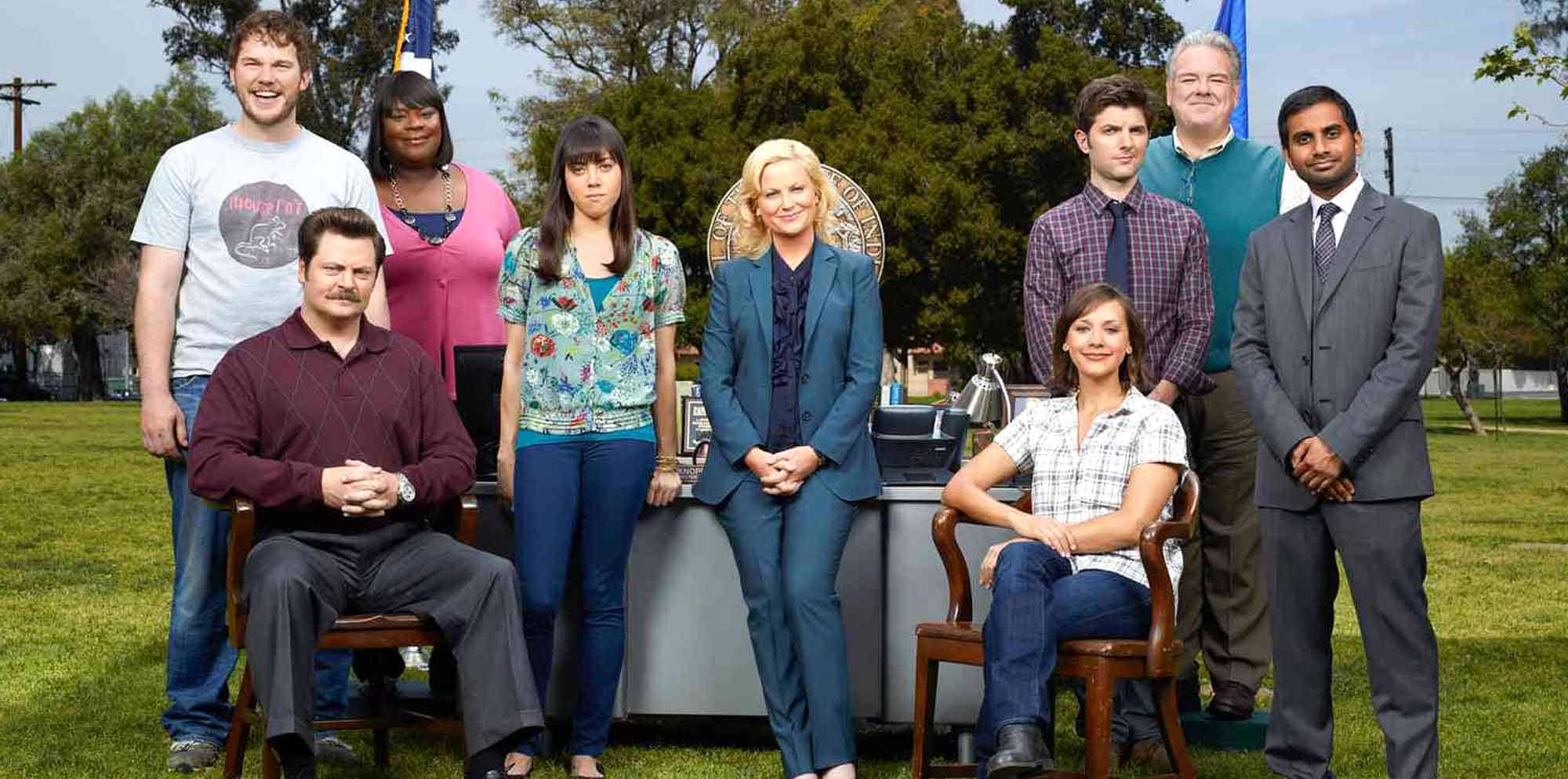 Funny, diverse cast of characters from "Parks and Recreation" standing outdoors in a park, showcasing teamwork and community.