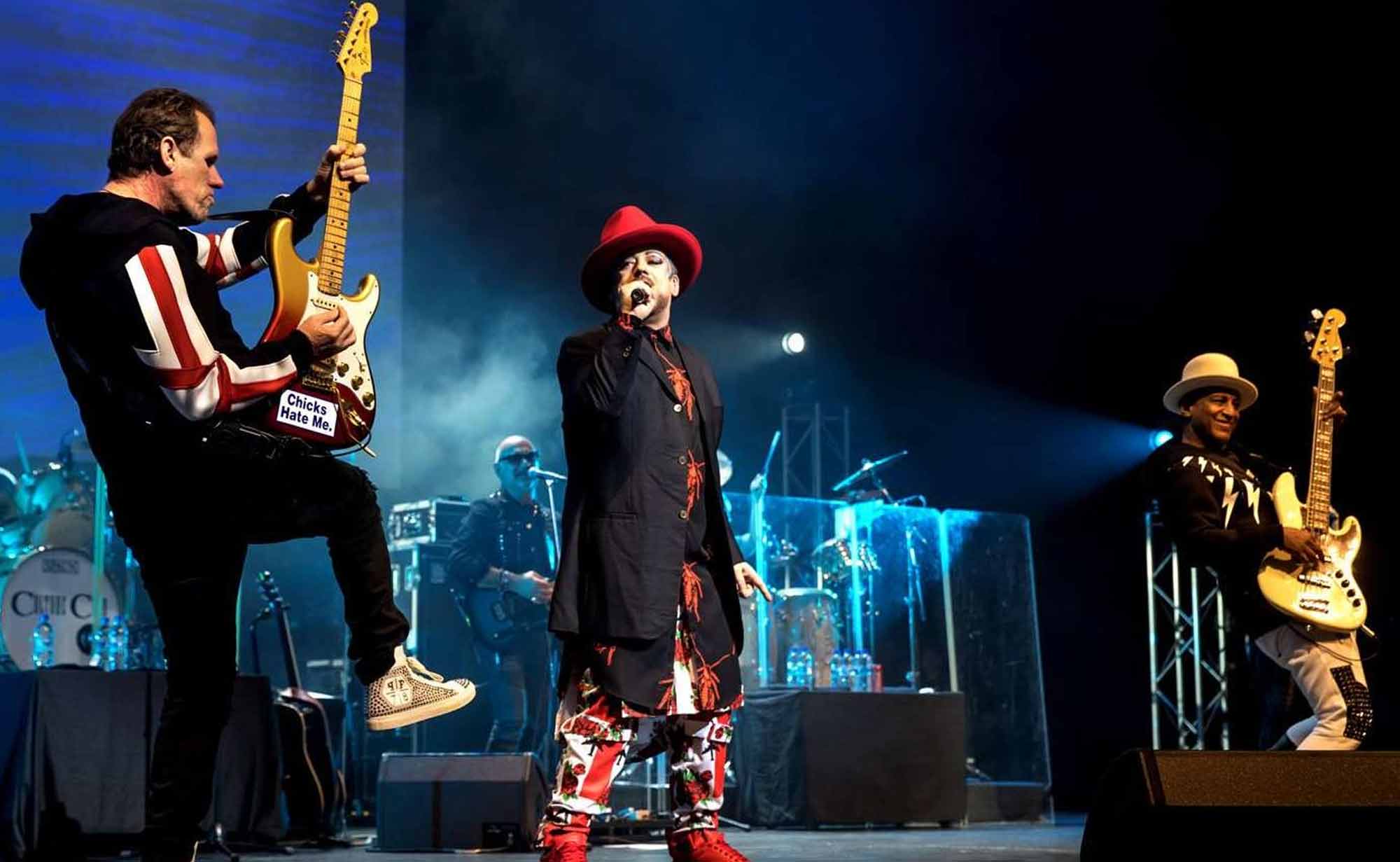 Artist performing on stage with guitar and microphones during a live concert event, emphasizing musical entertainment.