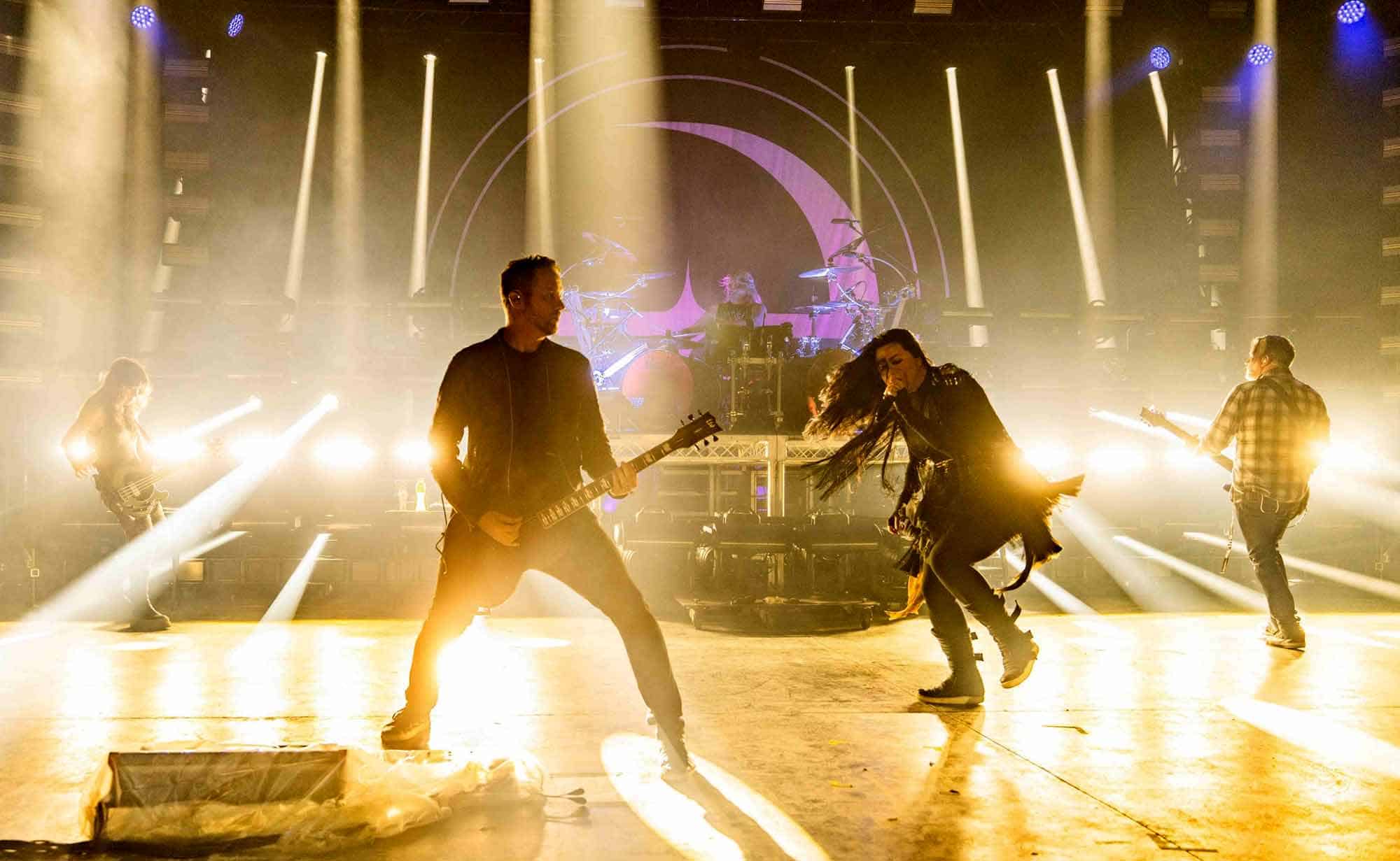 Guitarists and vocalist performing energetically on stage during a SocieTees concert with vibrant lighting effects.