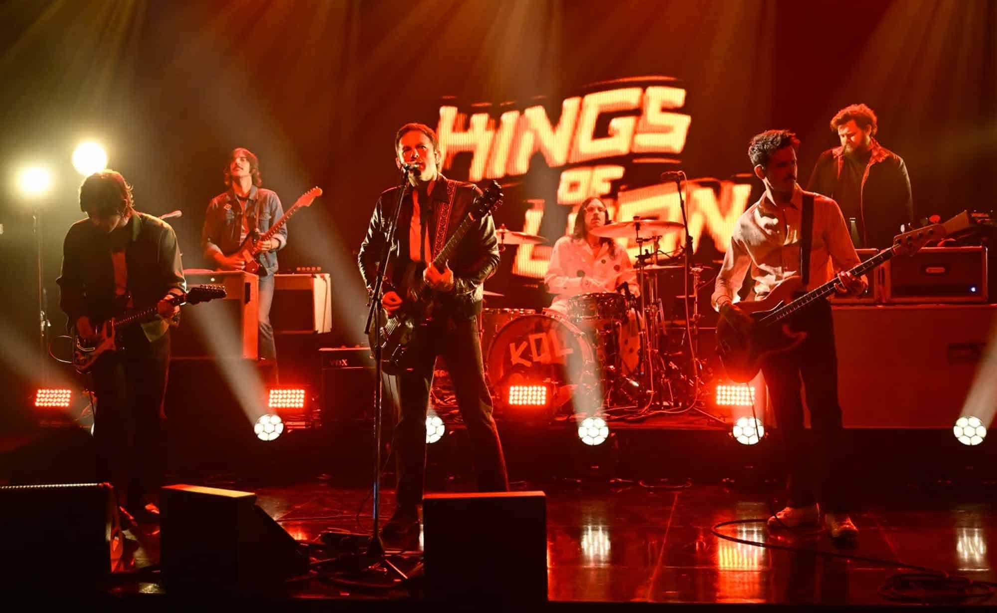 Energetic rock band on stage with colorful lights and "HINGS of THE" backdrop.