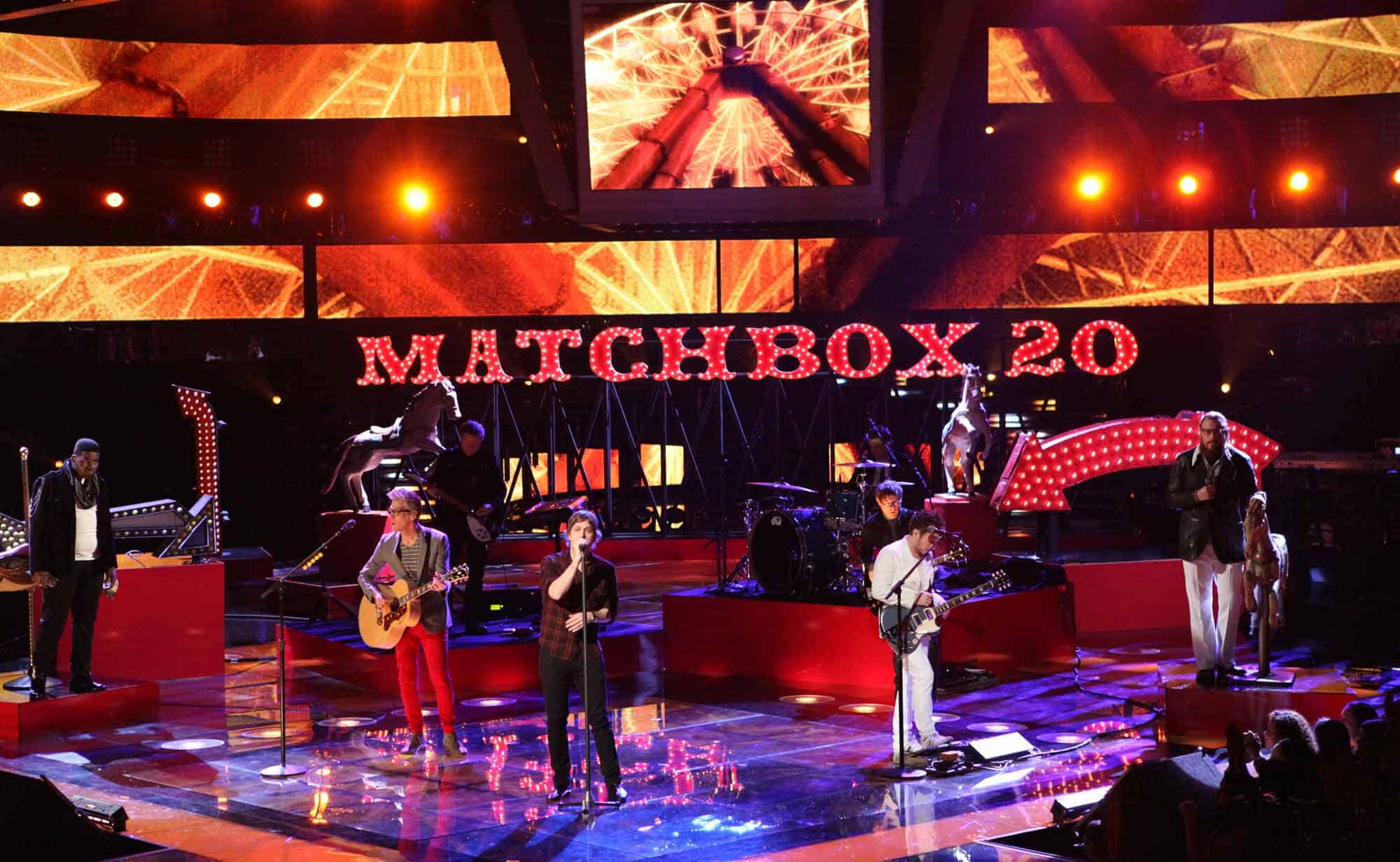 Bright stage with Matchbox 20 sign, band playing guitars, drums, and vocals during concert. Colorful lighting creates energetic atmosphere.