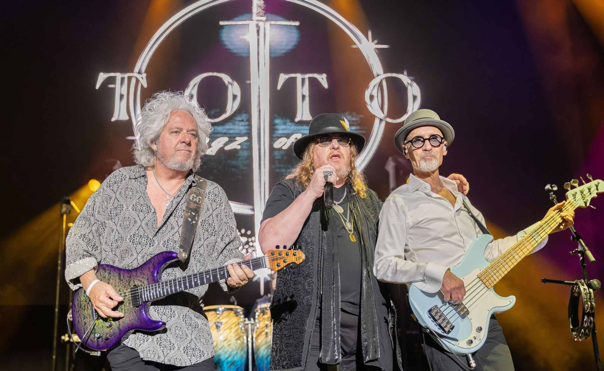 A legendary rock band performing on stage with guitars and microphones, featuring vibrant lighting and iconic logo backdrop.