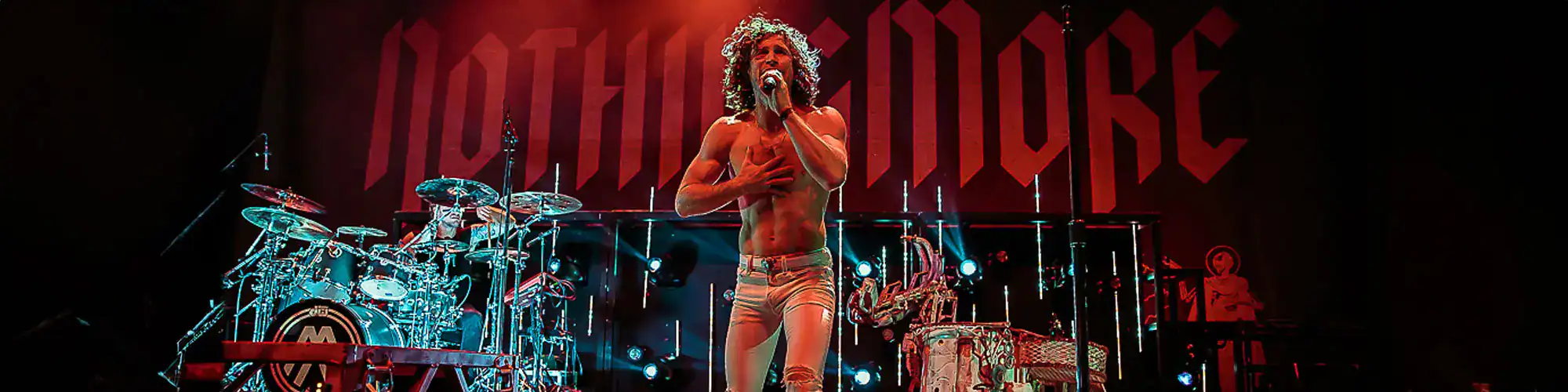 Energetic live music performance featuring a shirtless male singer with curly hair, bright stage lights, and a full band.