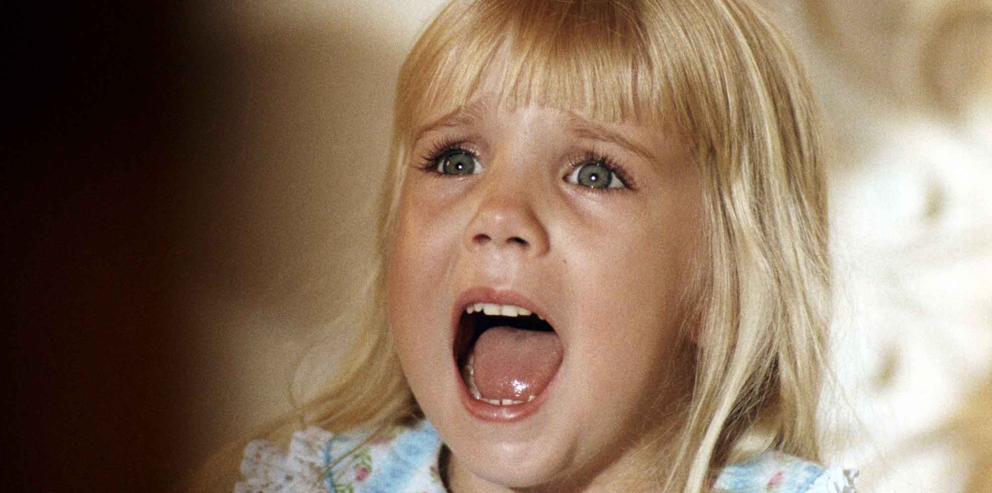Vivid image of a surprised young girl with blonde hair, big eyes, and an open mouth showing emotion.