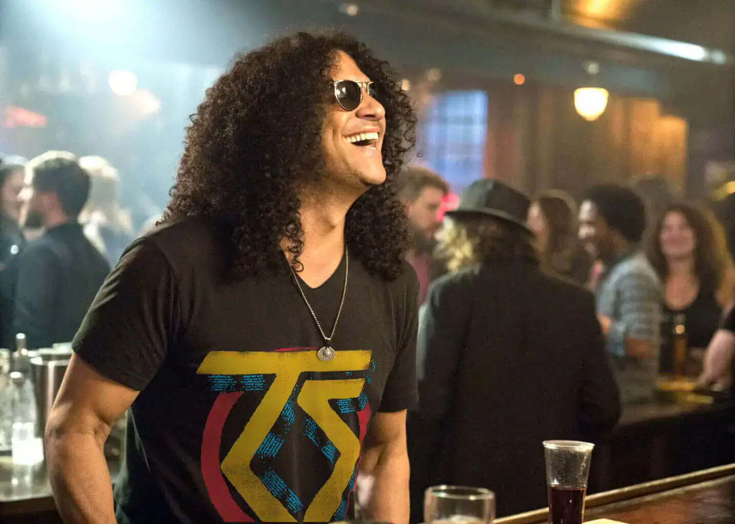 A rock fan with long curly hair and round sunglasses wearing a Twisted Sister Rock Band Logo Men's T Shirt