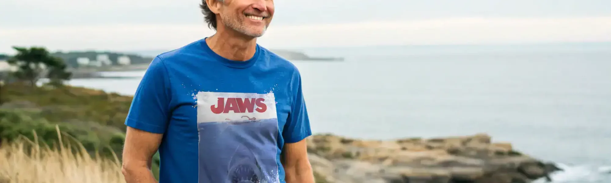 Portrait of a cheerful man wearing a Jaws movie T-shirt enjoying seaside scenery.