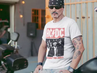 Male biker in AC/DC T-shirt with tattoos and sunglasses by motorcycle.