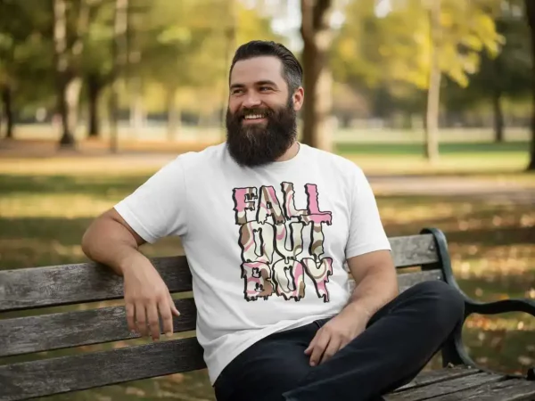 A man with a beard smiles while sitting on a park bench during fall, wearing a "Fall Out Boy" graphic T-shirt, surrounded by colorful autumn trees and a peaceful outdoor setting.