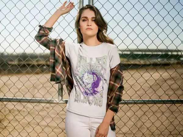 Stylish woman wearing a graphic tee with a horse design and plaid shirt, standing by a fence outdoors.